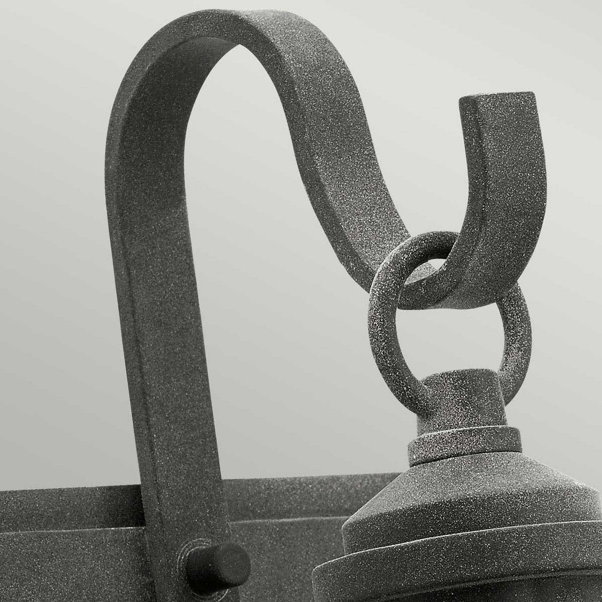 A close-up showcases the Riverwood Outdoor 1 Light Wall Lantern in Weathered Zinc, featuring a textured gray metal hook with a curved design that exudes a rustic seaside vibe. The lantern is attached to a ring, embodying nautical inspiration against a smooth gradient of light gray shades in the background.