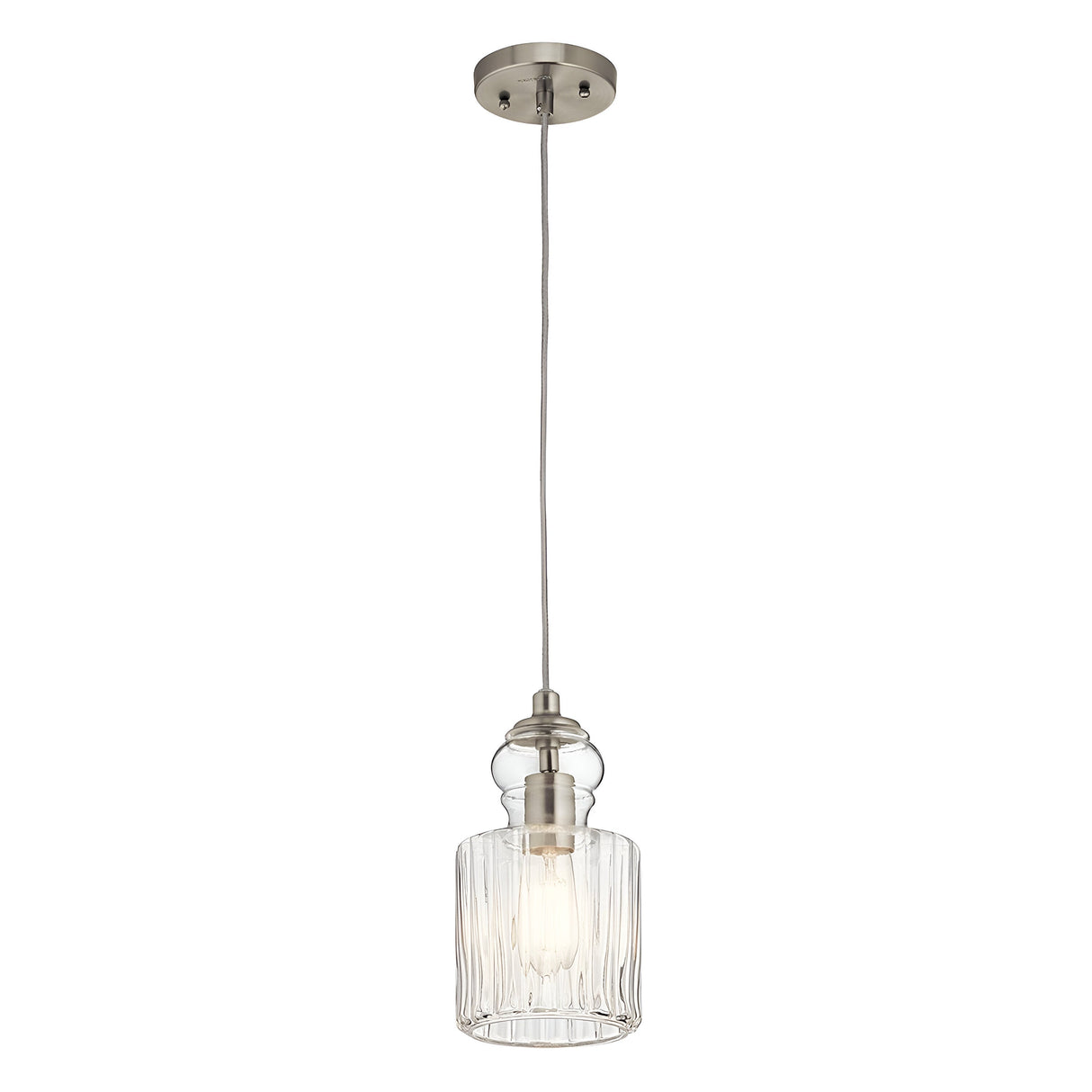 The Riviera-2 1 Light Pendant in Brushed Nickel is a vintage-inspired hanging light featuring a clear ribbed glass shade, ideal for kitchen island lighting. Its exposed bulb offers a warm glow, and the pendant is elegantly suspended by a cord from a circular ceiling mount.