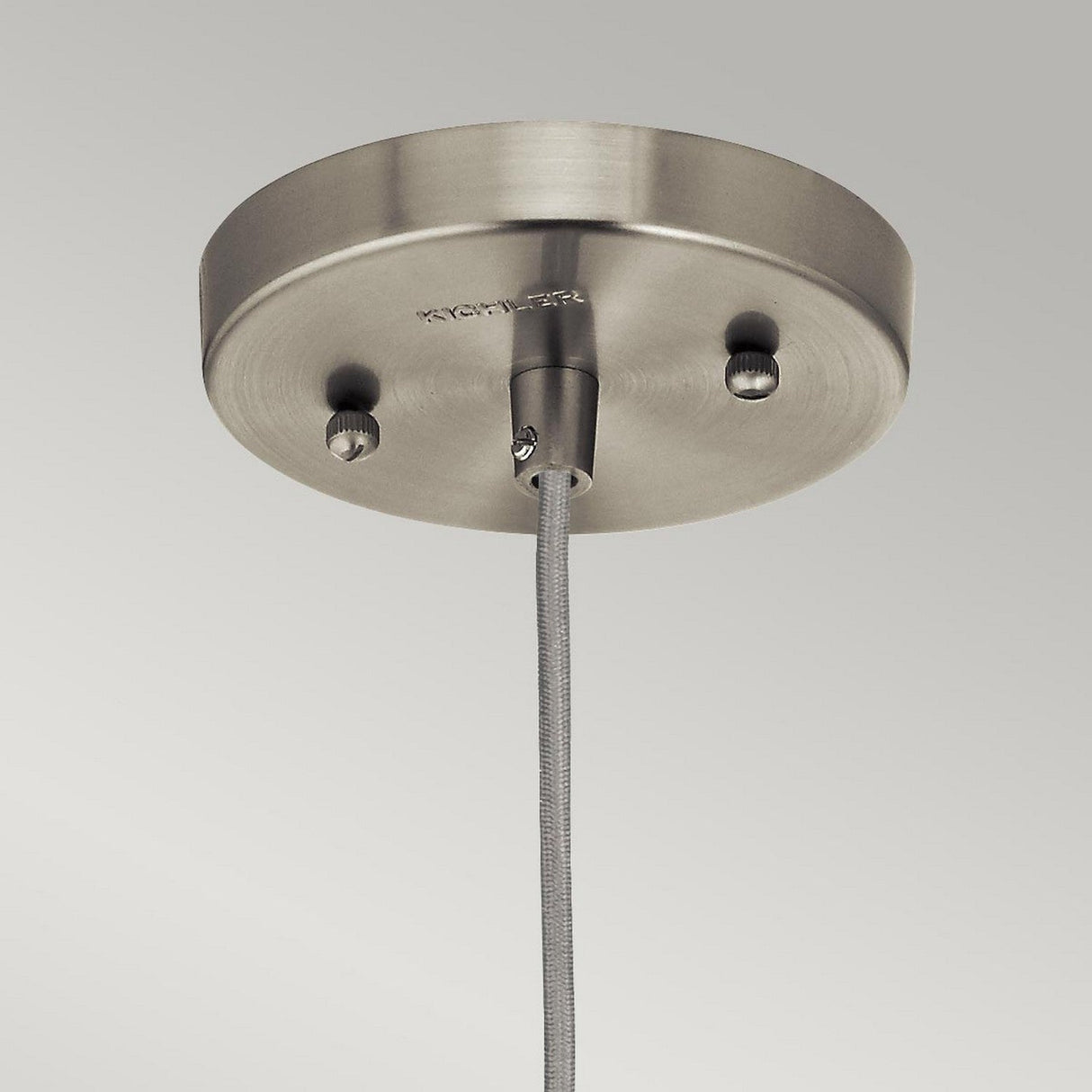 Close-up of the Riviera-3 1 Light Pendant with a vintage-inspired design, mounted on a ceiling. A cable extends from the center of its circular base, showcasing a brushed nickel finish against a light gray background.