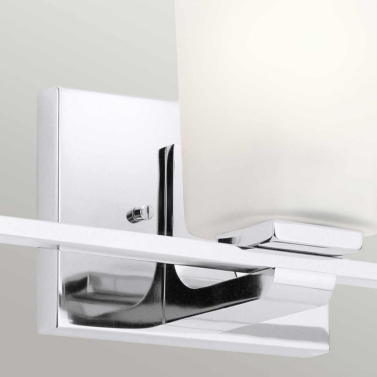 Close-up of the Roehm 3 Light Wall Light - Polished Chrome, showcasing its sleek rectangular design against a light gray wall. This fixture boasts a minimalist geometric shape with opal glass shades and a smooth, reflective surface.