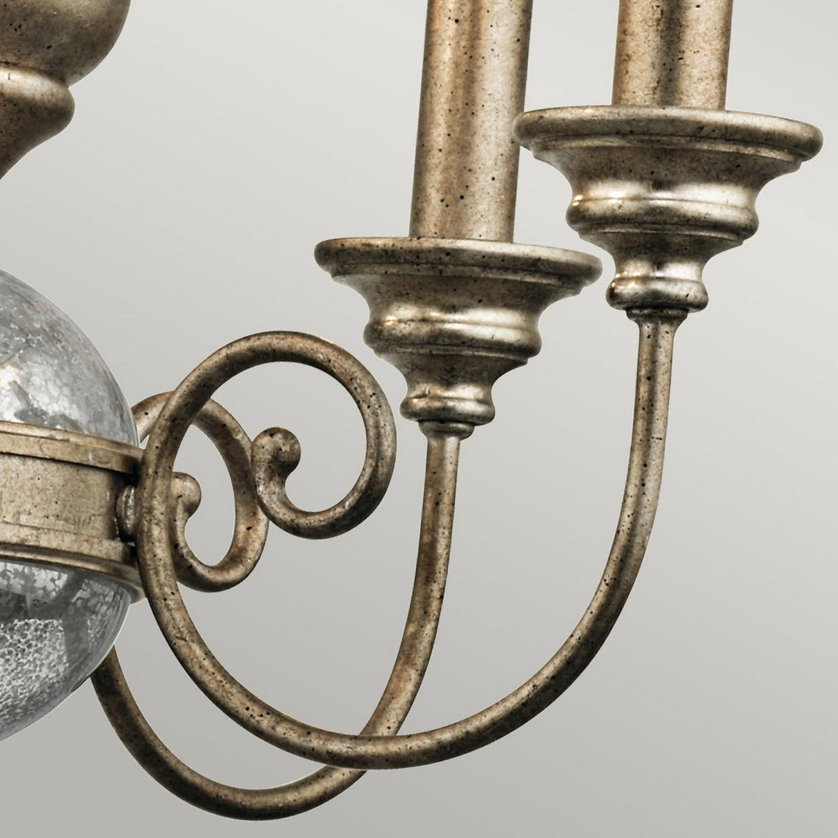 Close-up of the Rosalie 5 Light Mini Chandelier in a sterling gold finish, showcasing its ornate metallic design. It features two candle-like holders on elegantly curved arms and a decorative scrolling motif. The plain, light-colored background emphasizes the chandelier's antique elegance and craftsmanship.