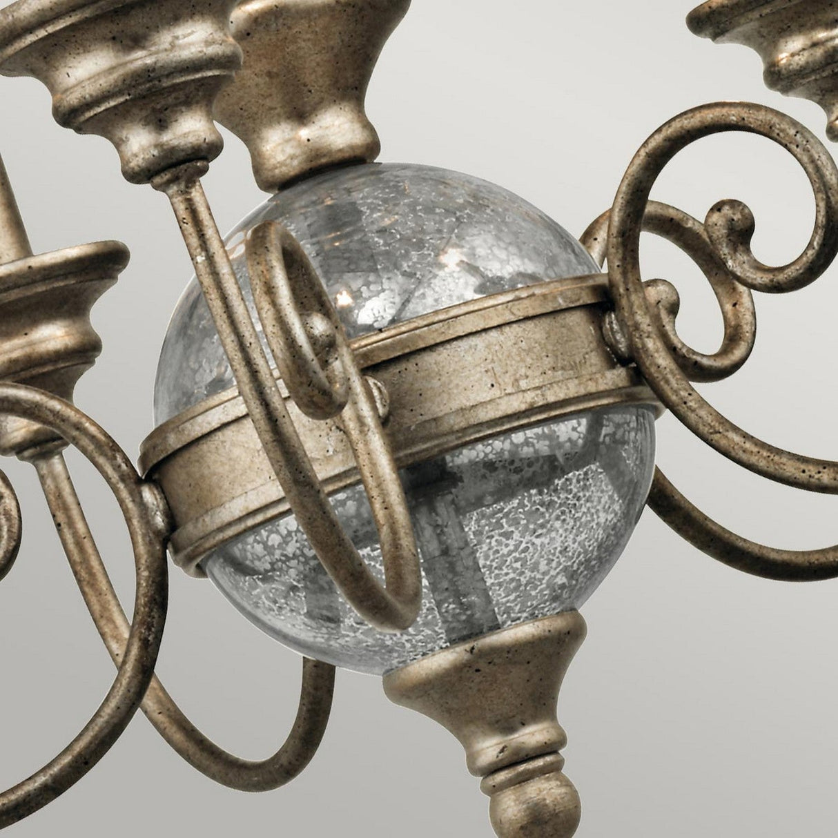 A close-up view of the Rosalie 5 Light Mini Chandelier in Sterling Gold showcases its shimmering glass orb and intricate metalwork. The ornate arms elegantly curl around the centerpiece, made from Antique Mercury Glass, all set against a neutral background.