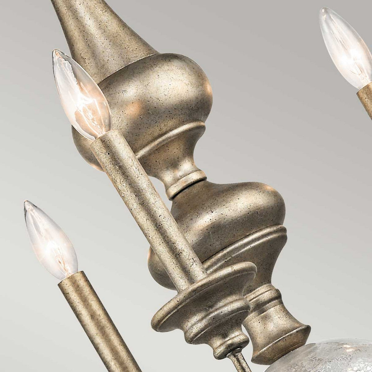Close-up of the Rosalie 5 Light Chandelier in Sterling Gold, showcasing its ornate design with multiple candle-shaped lights. The fixture boasts a textured, antique finish inspired by Williamsburg design and elegant elements, set against a neutral gray background.