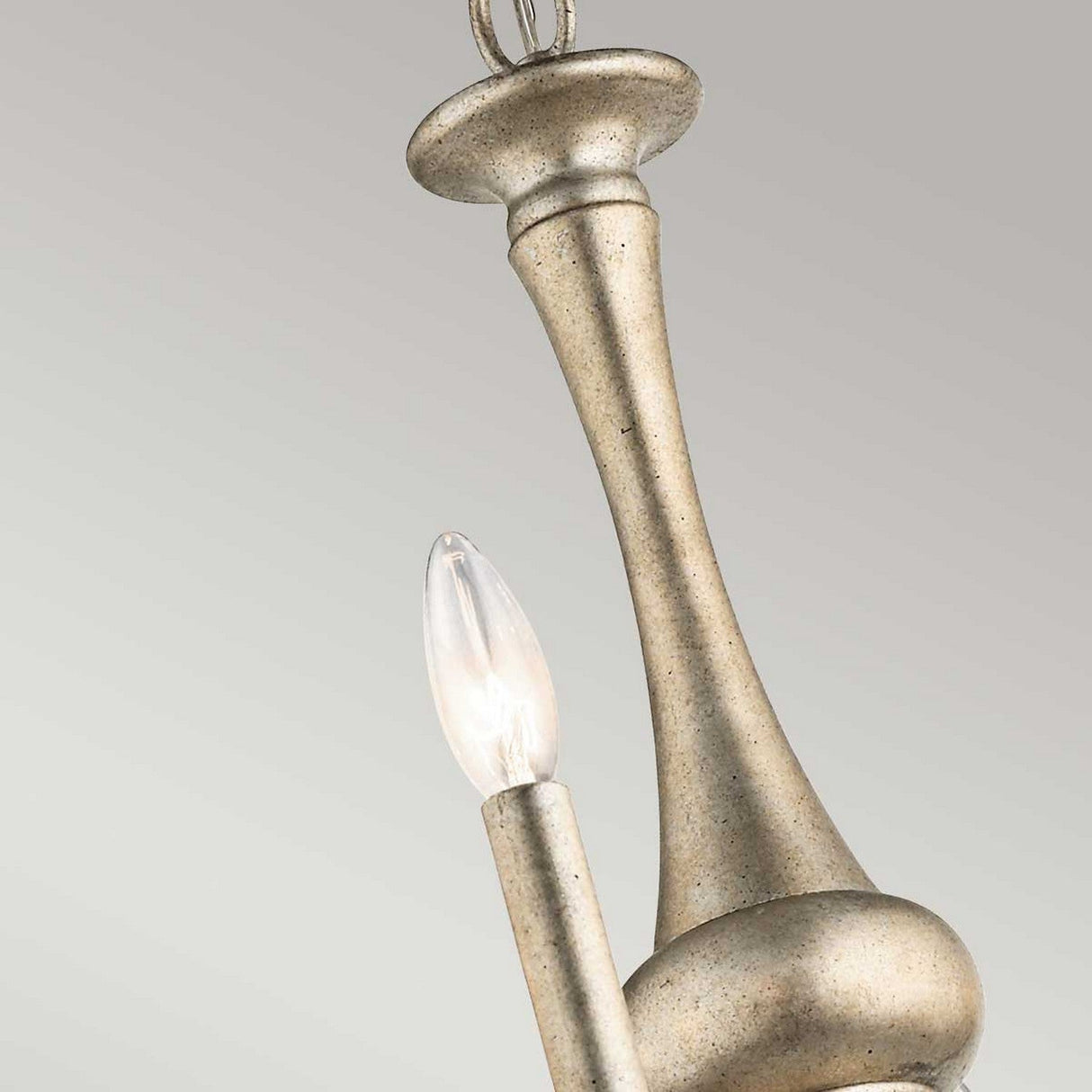 A close-up of the Rosalie 8 Light Chandelier in Sterling Gold, showcasing its silver metallic finish reminiscent of Williamsburg design, with a tall and slender stem. A single candle-shaped bulb protrudes from the fixture against a neutral gray background.