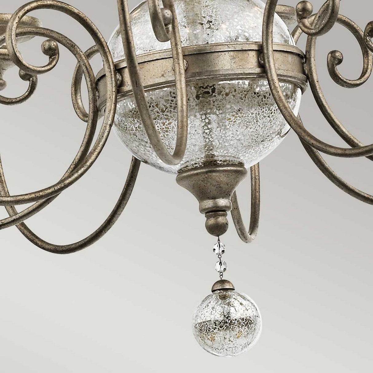 The Rosalie 8 Light Chandelier in Sterling Gold features intricate metal scrollwork and a large textured glass globe that evokes Williamsburg design. A smaller matching ornament made of antique mercury glass is suspended beneath, connected by a short chain.