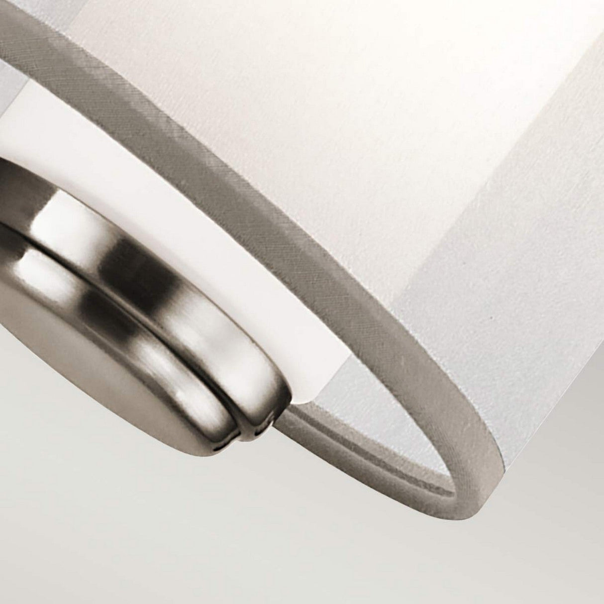 Close-up image of the Saldana 1 Light Wall Light - Silver, featuring a silver metal base and an opal glass cylindrical lampshade. The photo highlights the curvature and texture of the lampshade against a light background.