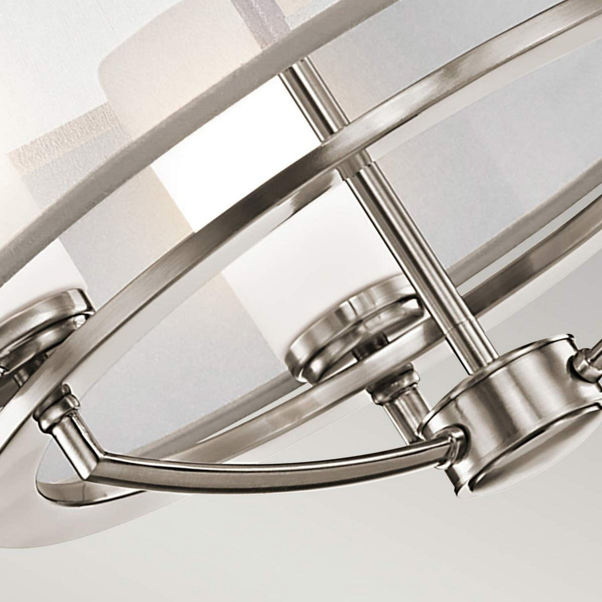 Close-up of a modern ceiling light fixture with a brushed nickel finish. The Saldana 3 Light Chandelier - Silver design showcases curved metal bars and frosted glass, offering a sleek and contemporary look.