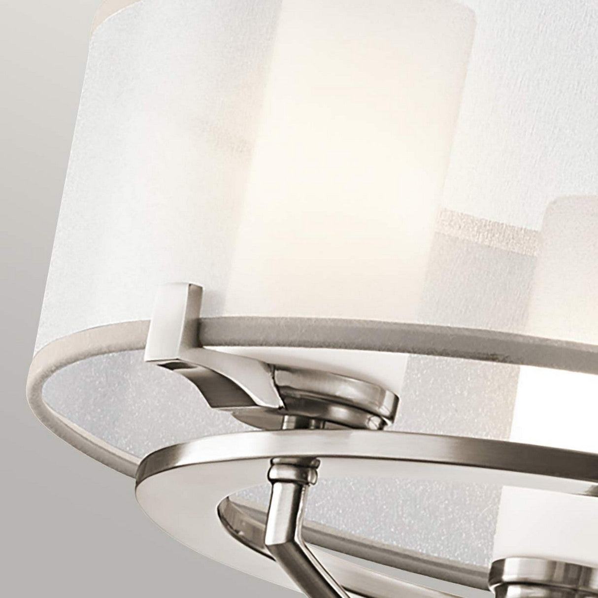 Close-up of the Saldana 3 Light Chandelier in silver, showcasing its white organza shade and metallic hardware. The design incorporates cylindrical elements, offering a sleek and contemporary aesthetic against a soft, muted background.