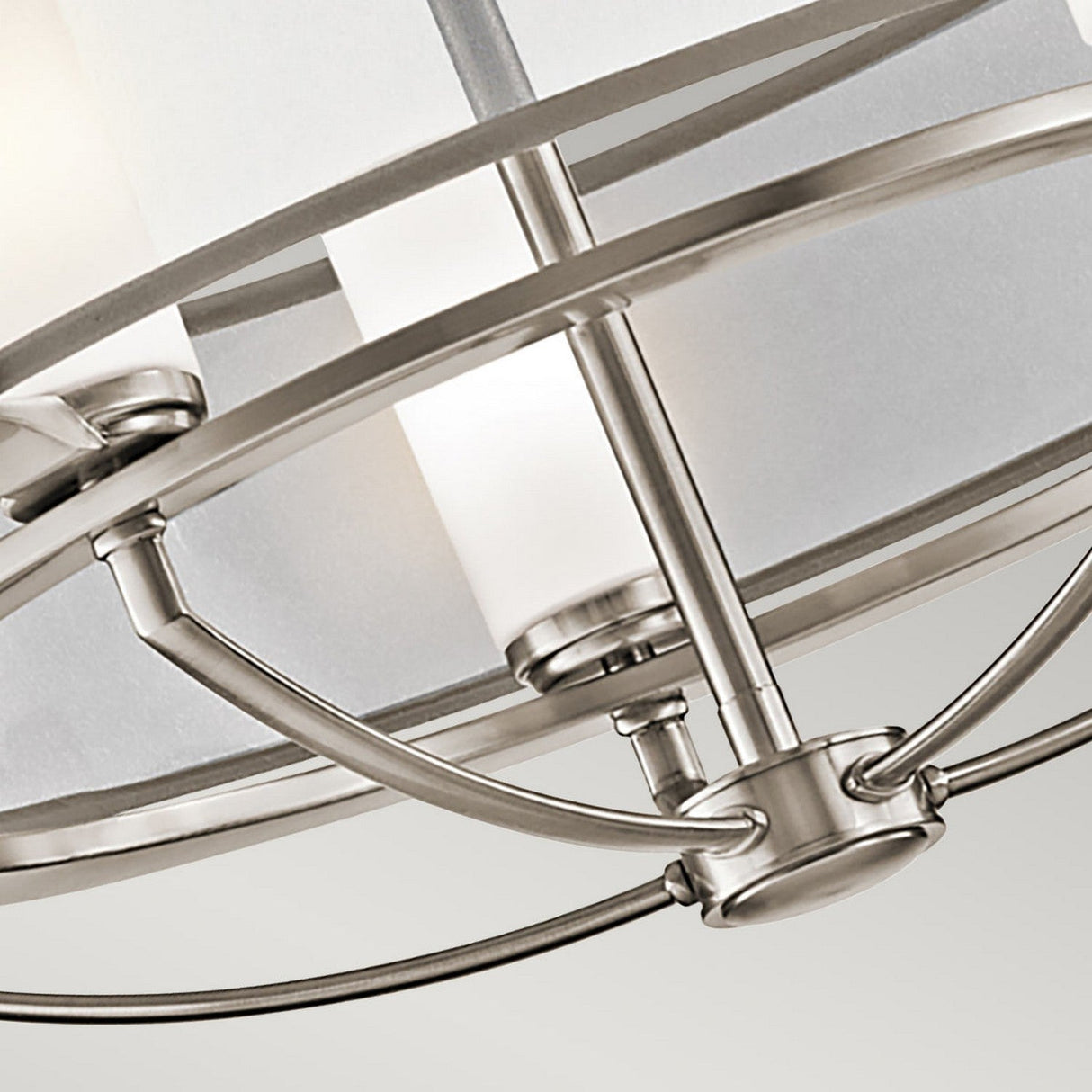 A close-up of the Saldana 5 Light Chandelier - Silver showcases its modern ceiling fixture with a five-light layout and cylindrical frosted glass shades against a white ceiling. The design highlights clean lines, a metallic frame, and a brushed nickel finish, reminiscent of an elegant silver chandelier.