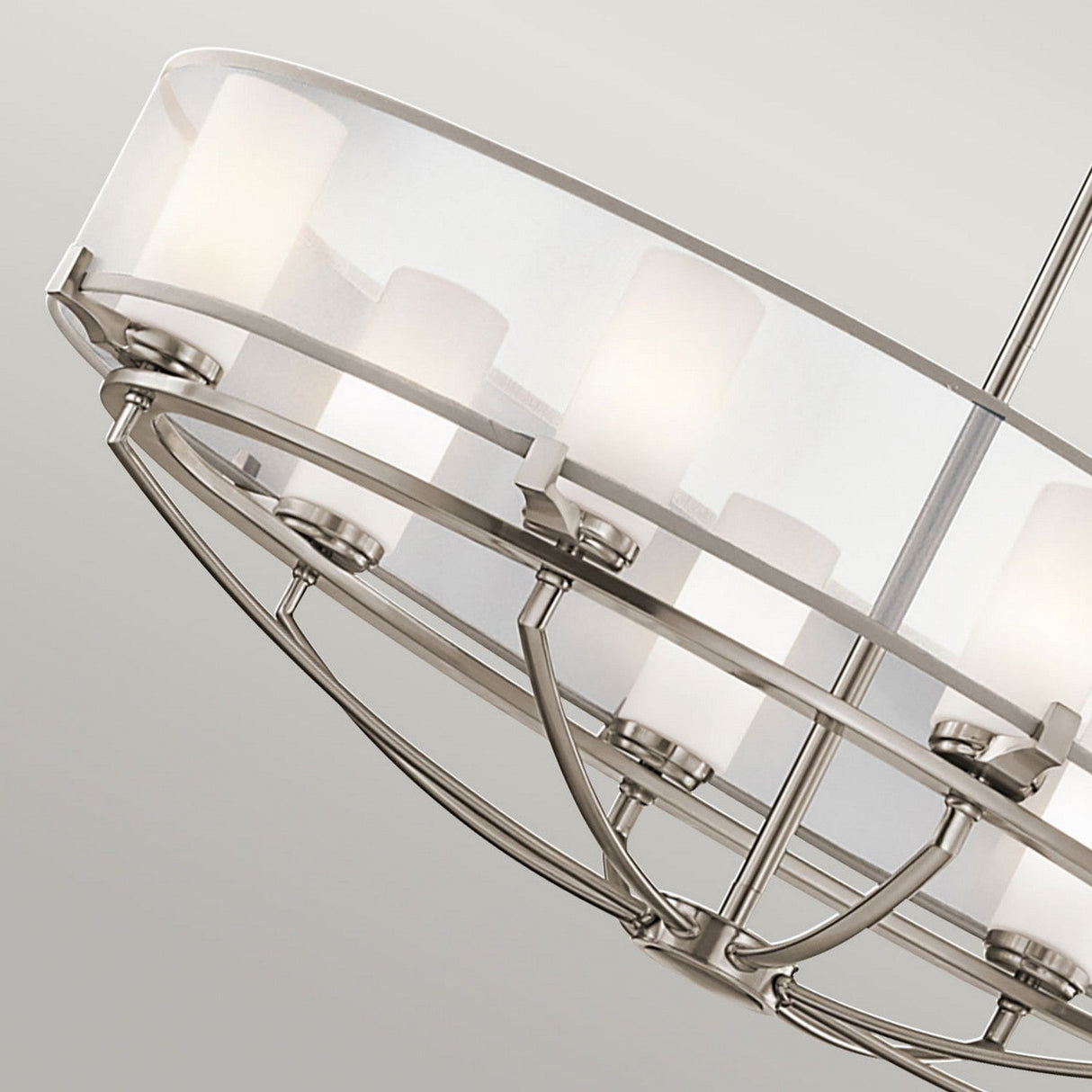 The Saldana 8 Light Oval Chandelier - Silver is a celestial-inspired lighting piece with a circular frame and frosted white cylindrical shades, showcasing a brushed metal finish and clean lines as it hangs elegantly against a light gray background.