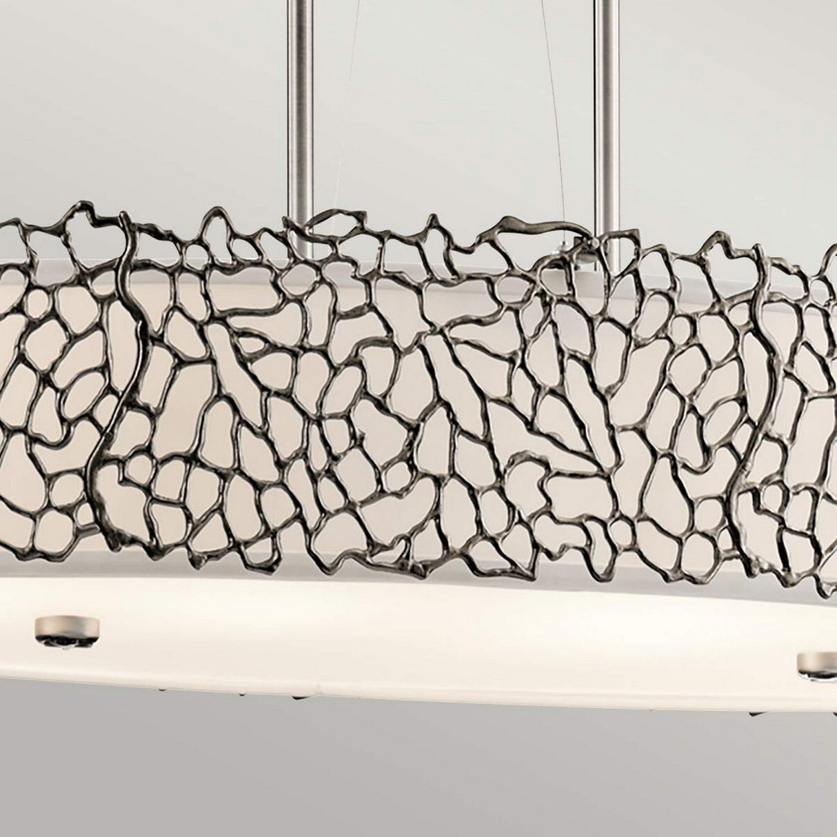 The Silver Coral 4 Light Oval Island Suspension - Silver showcases a contemporary design with an abstract, textured metal frame surrounding four white circular light fixtures. When placed against a neutral gray backdrop, it elegantly accentuates the detailed craftsmanship of the metalwork.