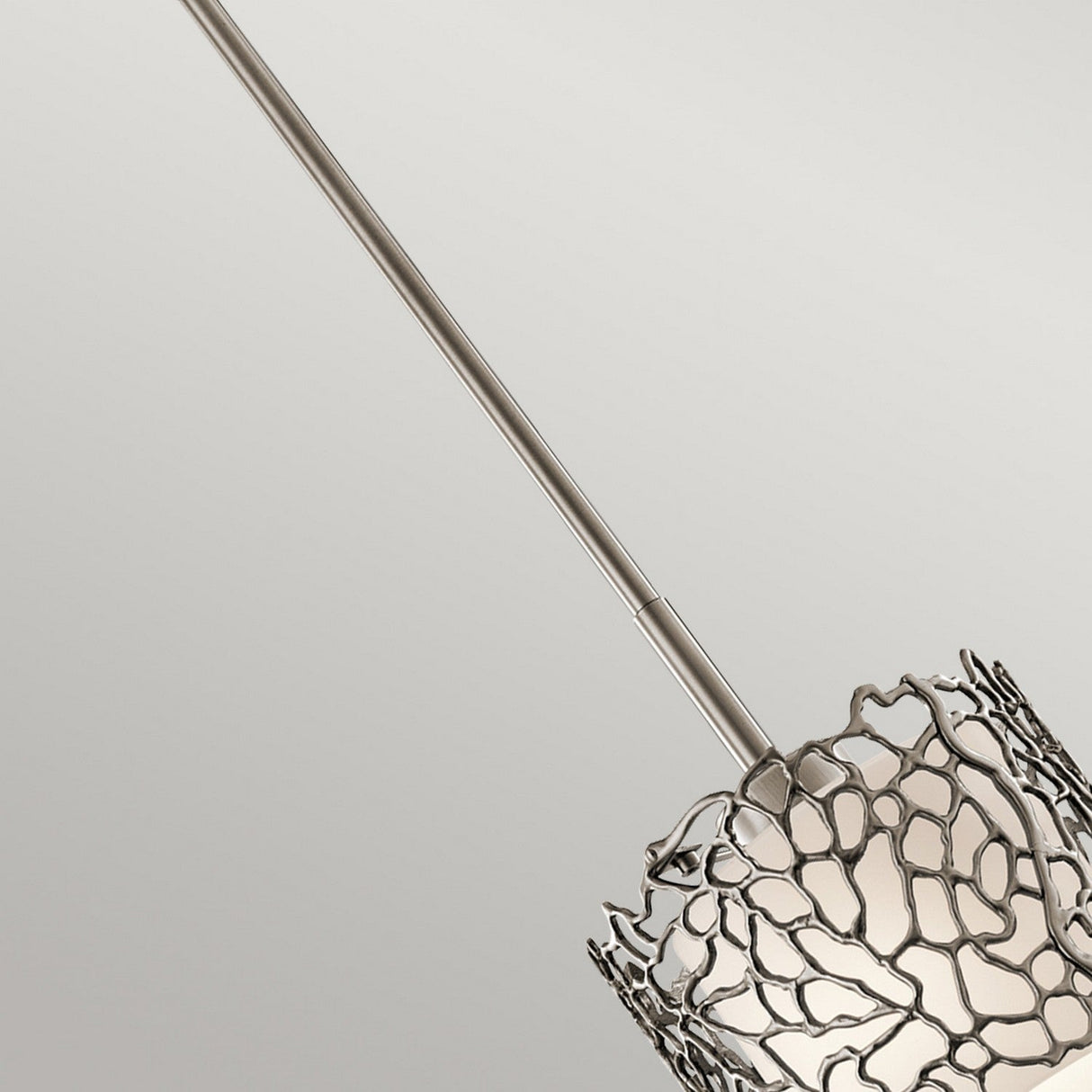 The Silver Coral 1 Light Mini Pendant - Silver features a contemporary metallic web-like design enveloping a white bulb, radiating nature-inspired elegance. Positioned diagonally against a light gray background, it brings a modern touch to any room.