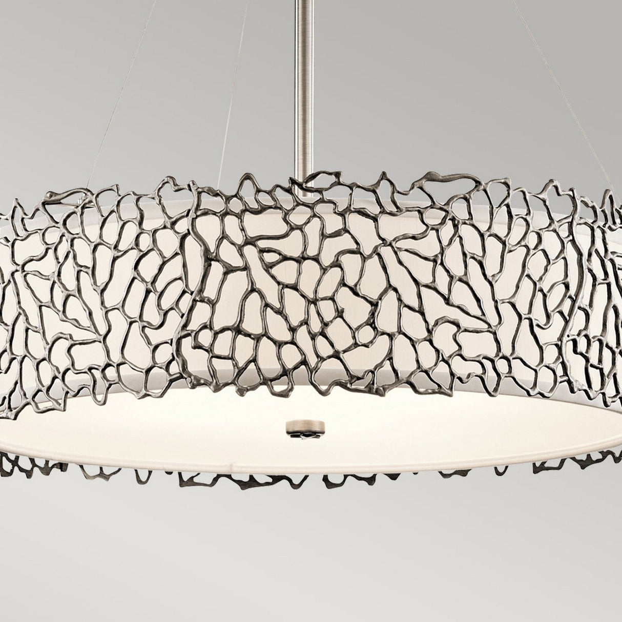 The Silver Coral 4 Light Drum Pendant - Silver features a modern chandelier design with a circular white shade, beautifully encased in an artistic, silver coral-inspired pattern. It hangs gracefully from a central rod against a simple backdrop, capturing nature-inspired elegance.