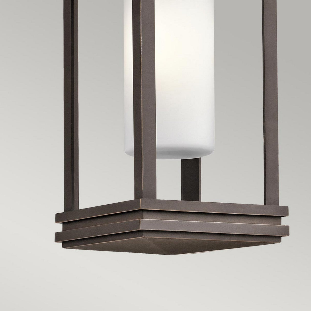 This is a detailed view of the South Hope Outdoor 1 Light Small Chain Pendant, showcasing its satin-etched cased opal glass in a sleek cylindrical shape, beautifully encased within a rectangular metal frame finished in luxurious rubbed bronze.