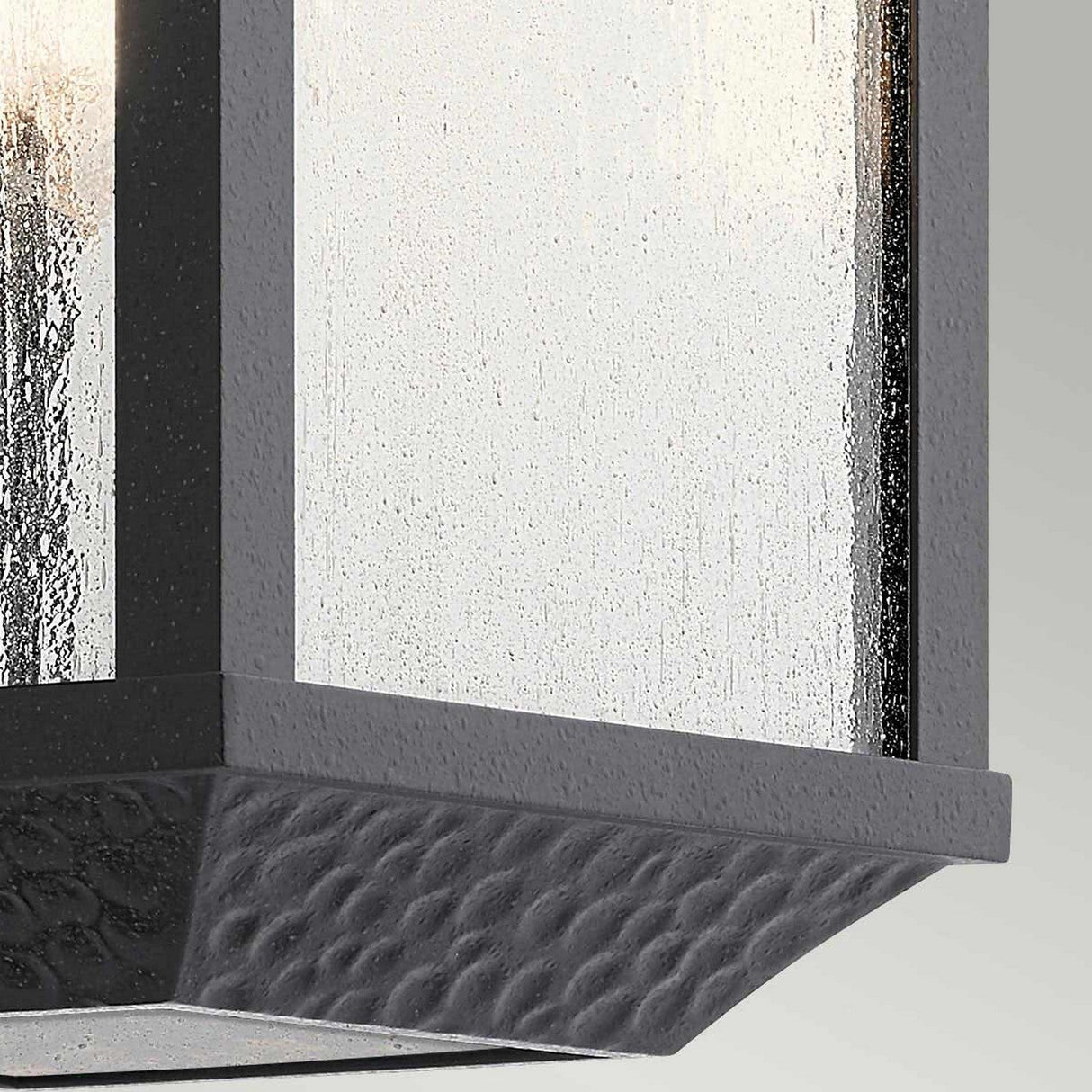 Close-up of the Springfield Outdoor 1 Light Medium Wall Lantern in black, featuring a textured, distressed finish and frosted seeded glass panel that reflects light. The design skillfully combines contemporary and classic elements, making it perfect for exterior home decor.