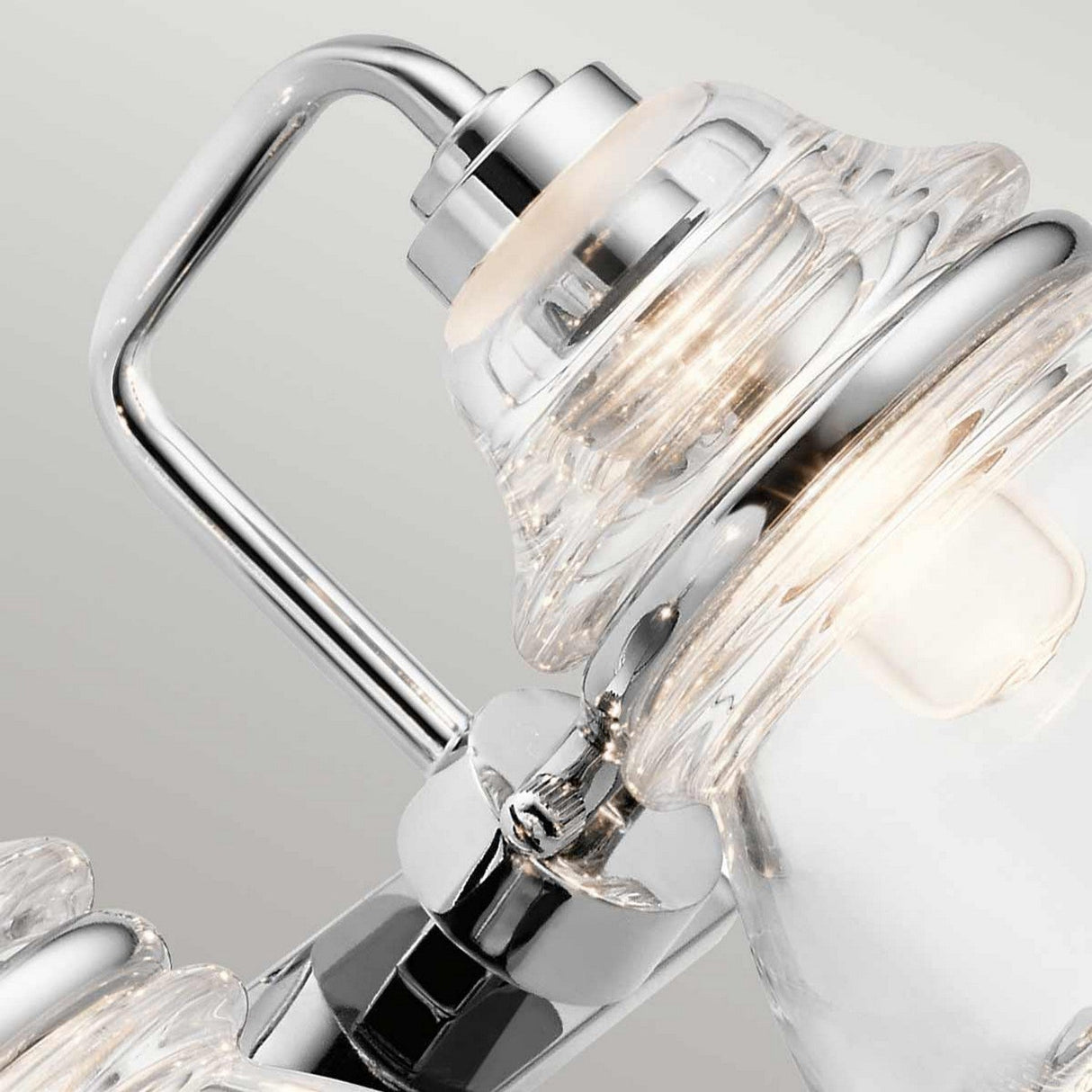 Close-up of the Talland 2 Light Wall Light in polished chrome, highlighting its elegant handle and illuminated features. The wall light showcases a sleek, modern design combined with vintage-inspired glasswork, complete with reflective surfaces and intricate detailing.