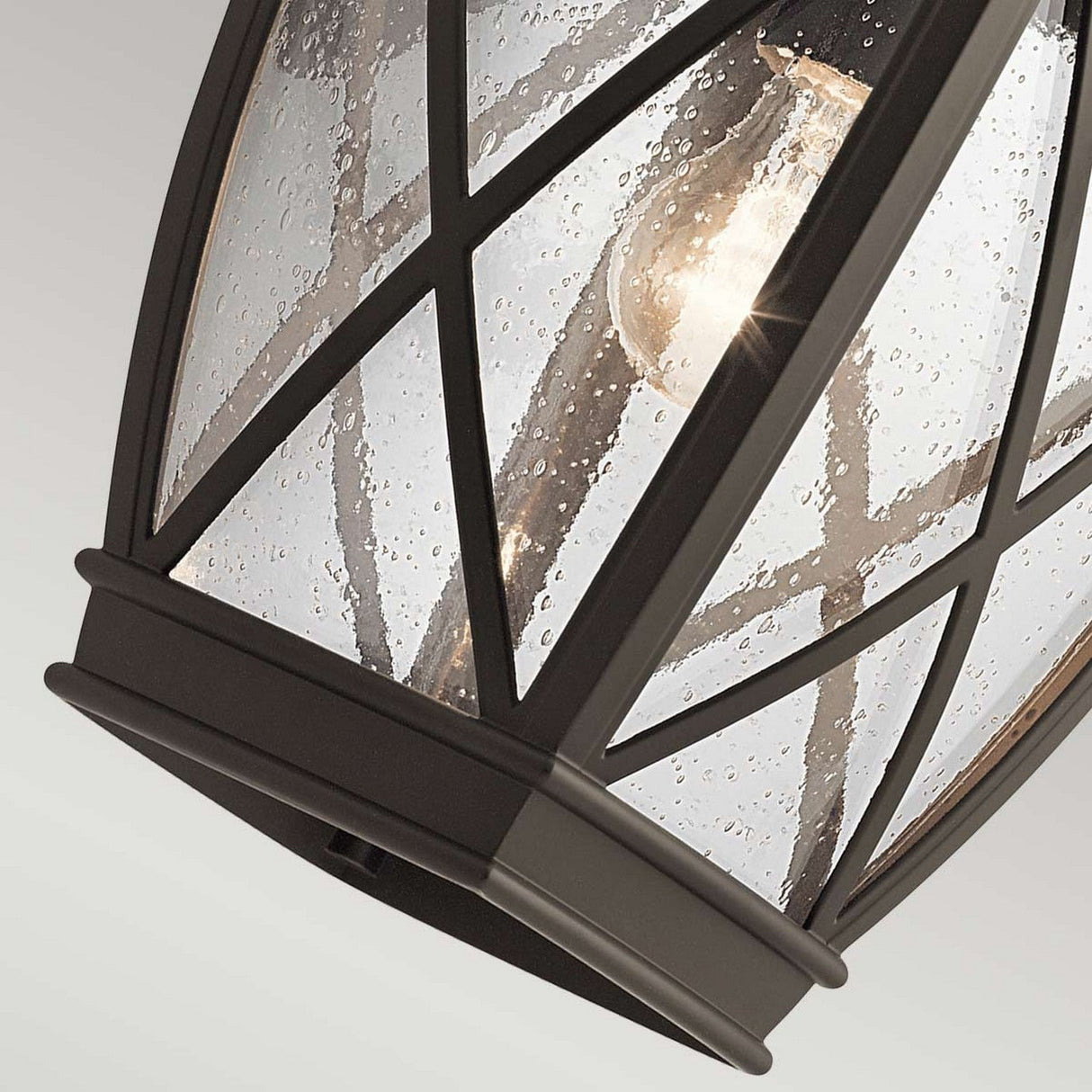 Close-up of the Tangier Outdoor 1 Light Large Wall Lantern in Olde Bronze, showcasing a black metal frame and clear glass panes with a vintage-style bulb inside. The seeded texture of the glass produces a speckled effect reminiscent of the classic design.