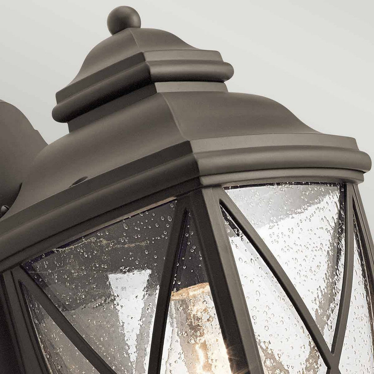 Close-up of the Tangier Outdoor 1 Light Medium Wall Lantern in an Olde Bronze finish, showcasing a vintage-style black metal frame with clear glass panels adorned with water droplets. The classic top cap protects the inner light bulb, and its IP44 rating guarantees durability against the elements.