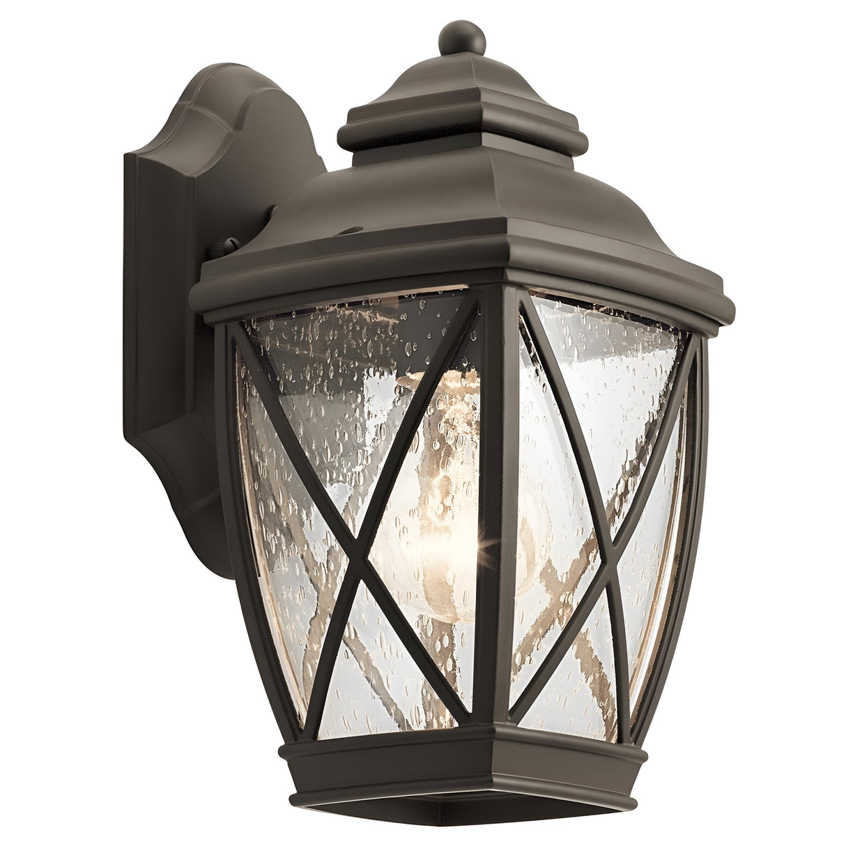 Introducing the Tangier Outdoor 1 Light Small Wall Lantern in Olde Bronze, featuring a classic design with clear, textured glass panels and a crisscross pattern. This decorative lantern is mounted on a wall bracket and beautifully illuminates its surroundings, adding charm to any setting.