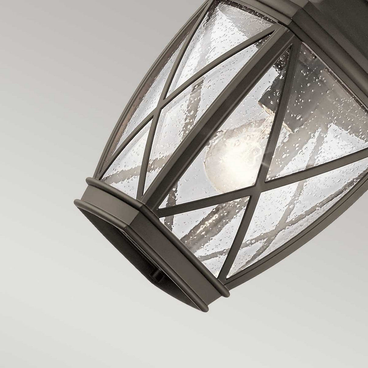 Close-up of the Tangier Outdoor 1 Light Medium Chain Pendant in an olde bronze finish, showcasing its clear, textured glass. The raindrop-like patterns on the glass reveal an incandescent bulb inside, while the fixture hangs at an angle against a gray background.