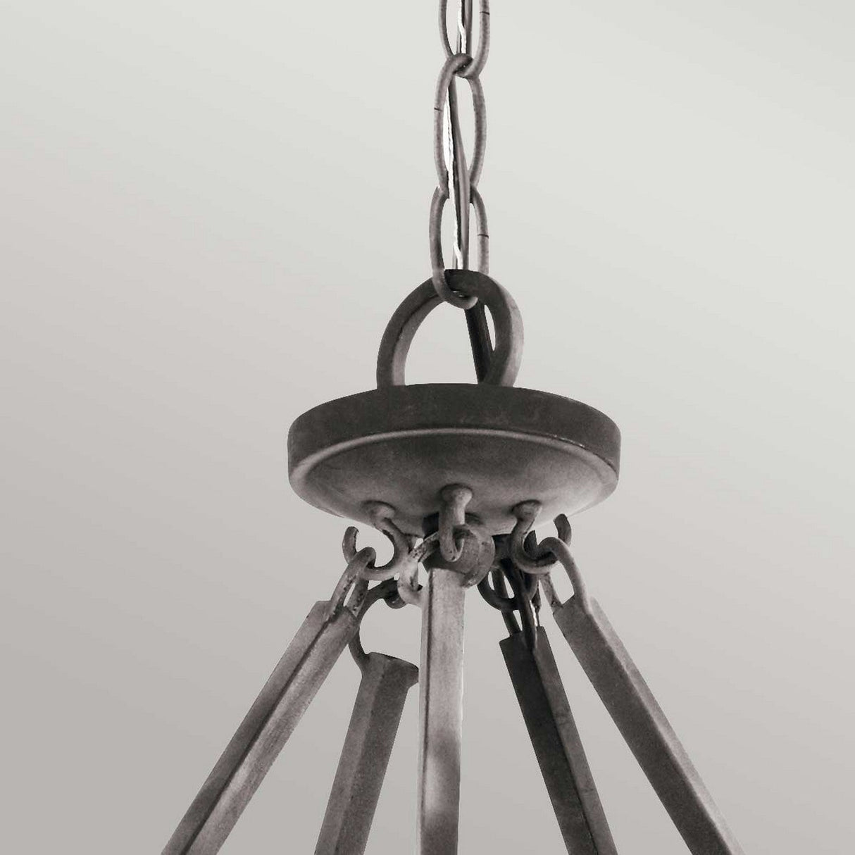 A close-up of the Taulbee 15 Light Chandelier in Weathered Zinc features its black metal and chain link design, set against a plain gray background. The focus on the upper part where the chains converge emphasizes its industrial style and rustic aesthetics.
