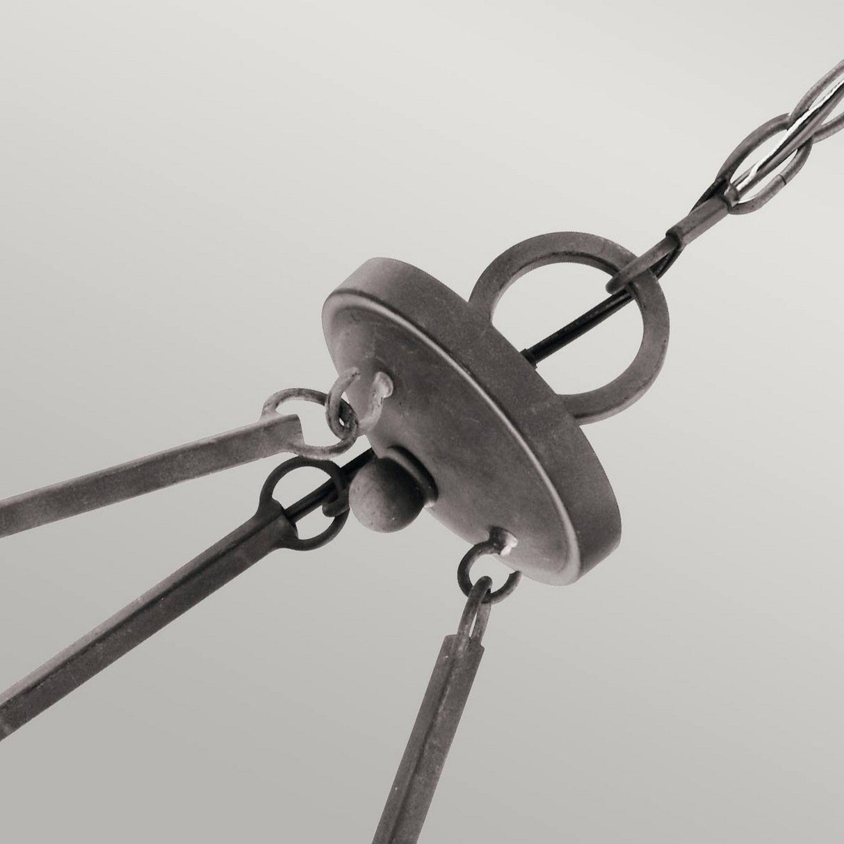 Close-up of the Taulbee 6 Light Chandelier in a lodge-inspired, industrial style featuring three metal rods connected to a circular base. Crafted from weathered zinc, the fixture includes a ring on top for attachment and is set against a neutral background.