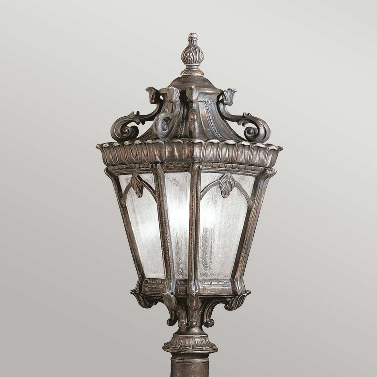 The Tournai 3 Light Extra Large Lamp Post in Bronze exudes timeless charm with its ornate detailing and frosted glass panels, standing elegantly against a neutral background.