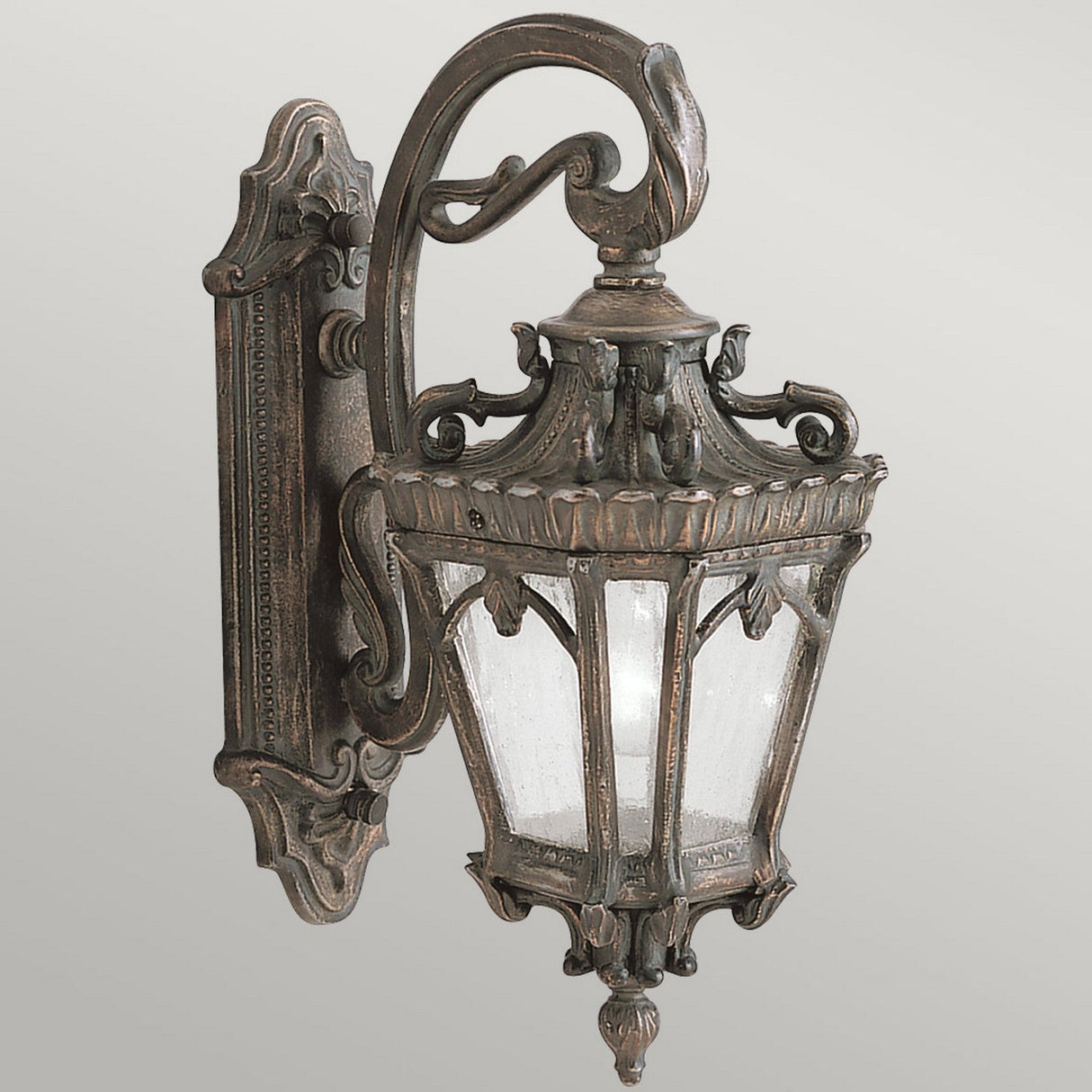 The Tournai Outdoor 1 Light Medium Wall Lantern in Bronze boasts vintage styling with ornate detailing and clear seedy glass panels. It features a curved arm and decorative backplate, making it perfect for enhancing your outdoor decor.