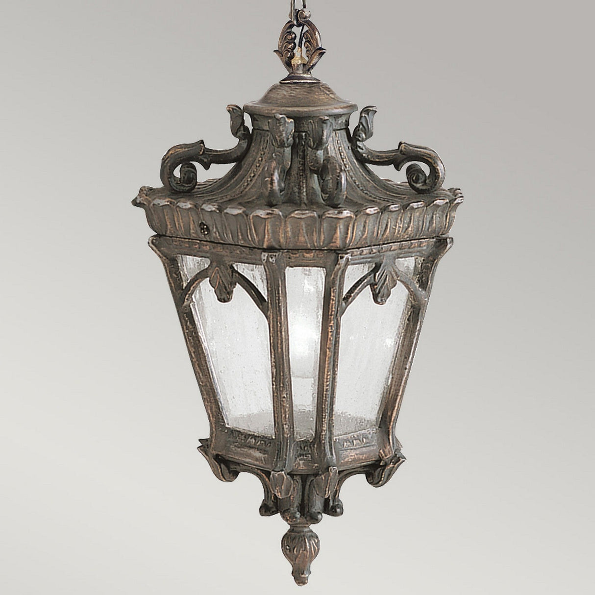 The Tournai Outdoor 1 Light Medium Chain Pendant in bronze showcases an ornate, vintage-style design with clear glass panels. Its intricate detailing on the top and base highlights elegant craftsmanship that evokes an antique aesthetic.