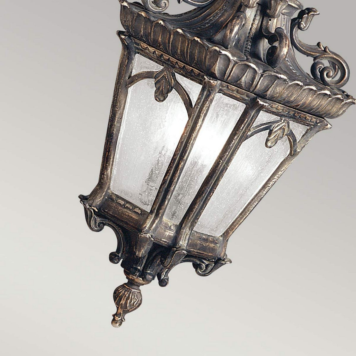 A close-up of the Tournai Outdoor 3 Light Extra Large Chain Pendant in bronze, featuring an antique-style lantern design with intricate metalwork and a leaf motif at the corners. It includes a decorative finial at the bottom and is suspended by a graceful bronze chain against a plain, light background.