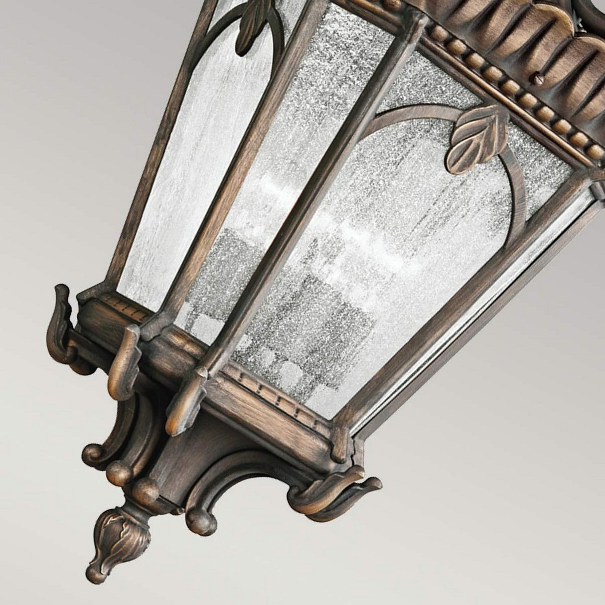 A close-up of the Tournai Outdoor 4 Light Grand Extra Large Chain Pendant showcases its ornate design with glass panels and a weathered bronze finish. The vintage style features decorative leaves and intricate detailing, giving this pendant a classic and elegant appearance.