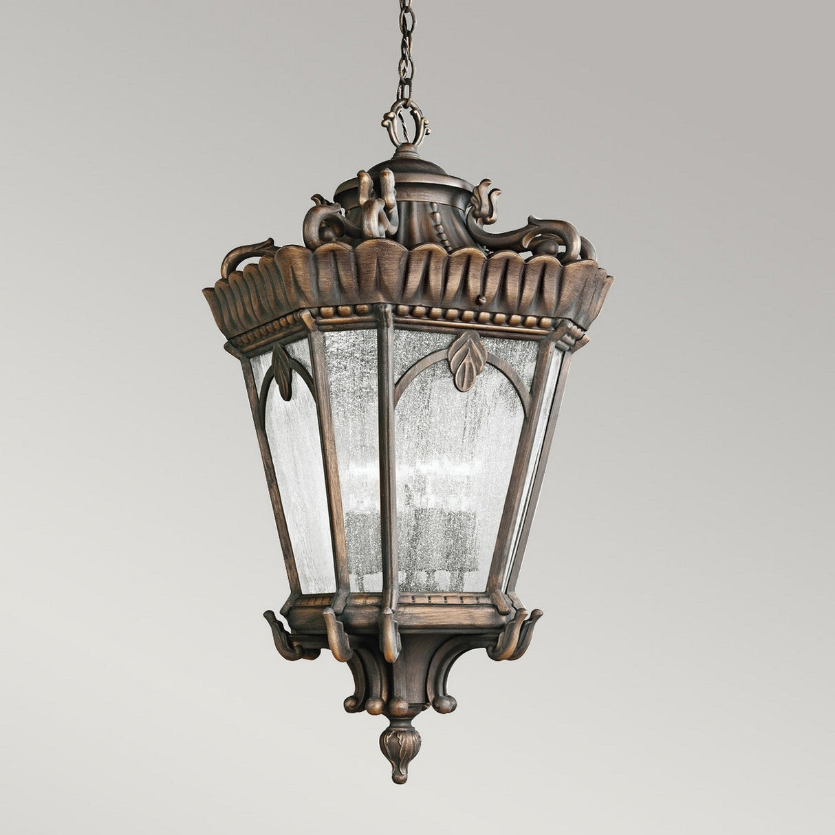 Introducing the Tournai Outdoor 4 Light Grand Extra Large Chain Pendant in Bronze, this exquisite fixture features a vintage design with a beautifully ornate finish and six glass panels. Suspended from its chain, it adds charm and elegance to any neutral backdrop with its decorative detailing.