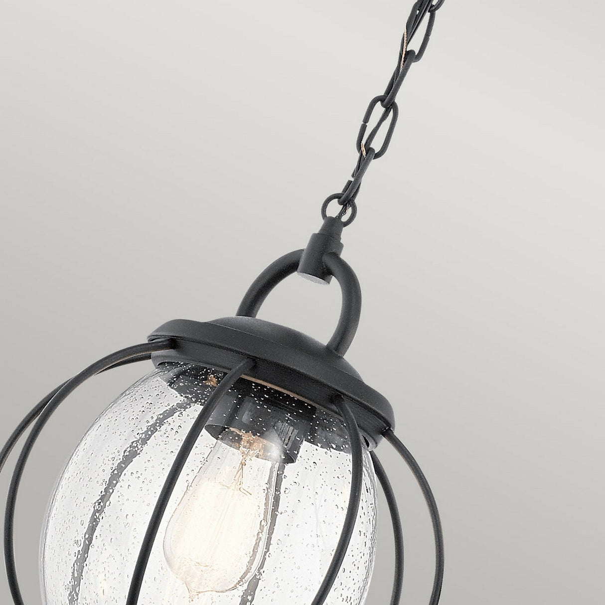 The Vandalia Outdoor 1 Light Medium Chain Pendant in black, featuring a contemporary design with clear seeded glass enclosing the bulb, is elegantly suspended by a chain against a plain light gray background as an outdoor lighting feature.