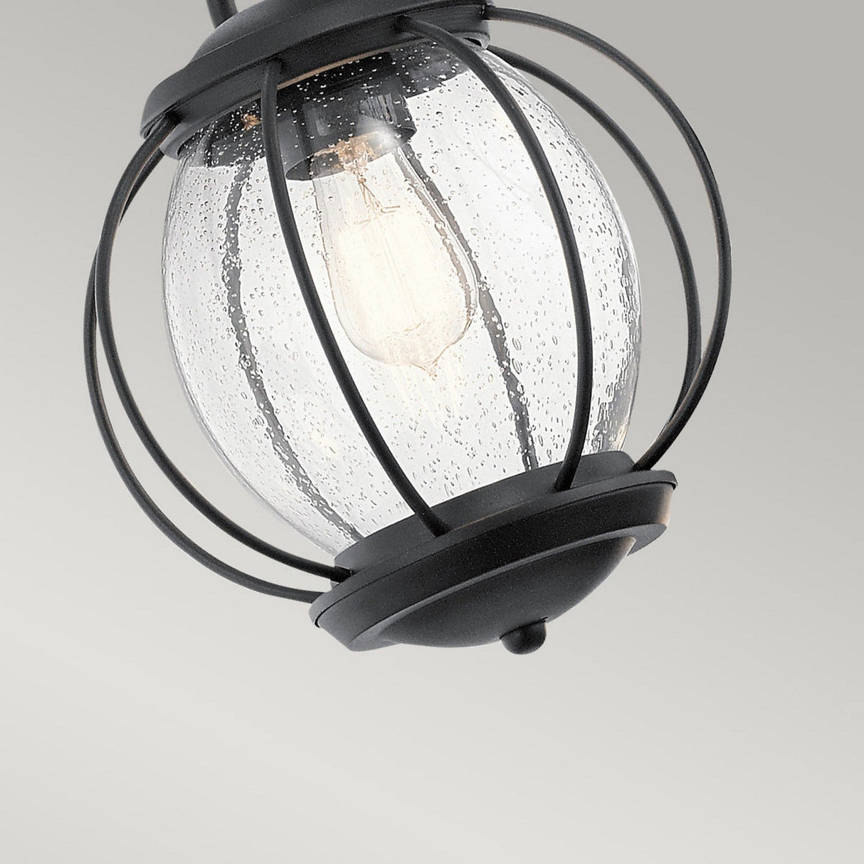A close-up of the Vandalia Outdoor 1 Light Medium Chain Pendant in black showcases a contemporary design with a clear, speckled glass globe encased in a sleek metal cage. The visible light bulb is suspended by a chain against a plain gray background.