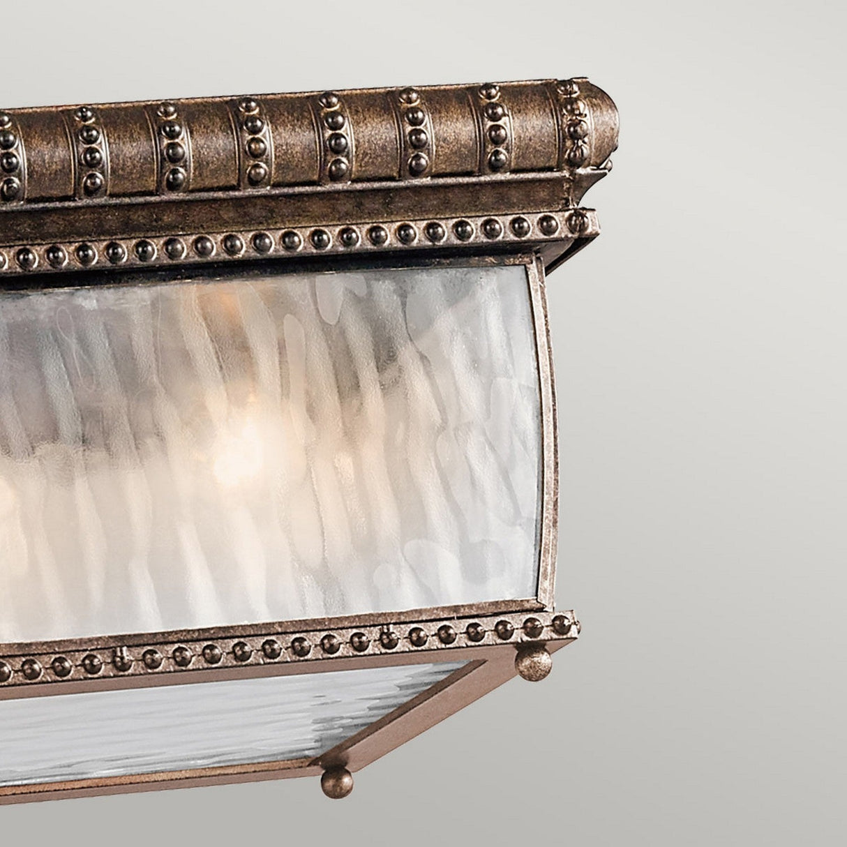 A close-up of the Venetian Rain Outdoor 2 Light Flush in Brushed Bronze showcases intricate metal detailing and frosted glass panels, adorned with a beaded design along the edges. This fixture exudes Italian Renaissance elegance against a neutral background.