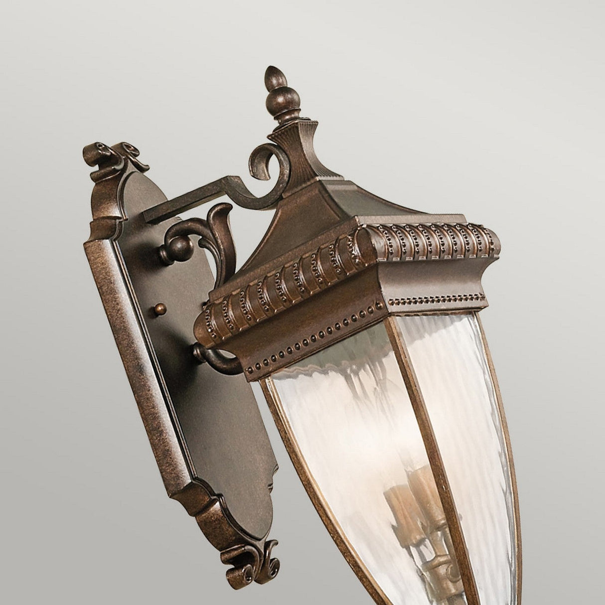 Presenting the Venetian Rain Outdoor 2 Light Medium Wall Lantern in brushed bronze, which boasts a vintage-style Italian design with decorative detailing. This elegant fixture features clear, beveled glass panels mounted on an ornate backplate, exuding an antique aesthetic.