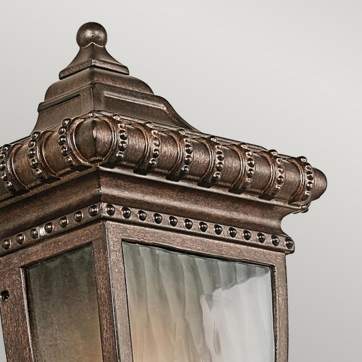 A detailed view of the Venetian Rain Outdoor 1 Light Half Wall Lantern reveals its decorative ornate metalwork and frosted glass panels. The lantern's textured brushed bronze finish exudes elegance with intricate detailing around the edges.