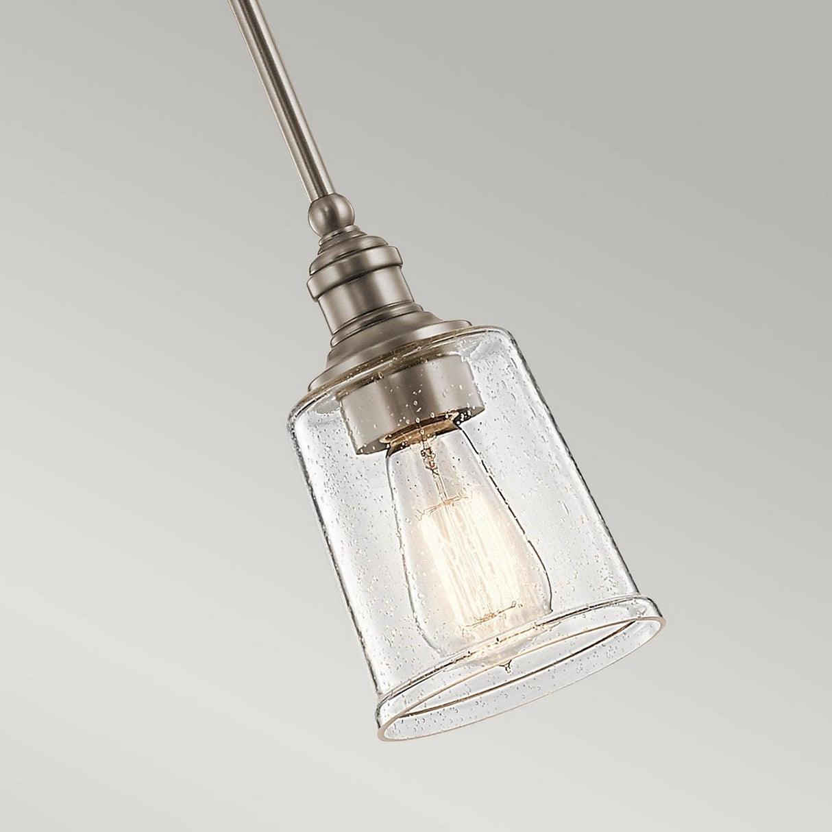 The Waverly 1 Light Mini Pendant - Silver showcases a vintage and industrial aesthetic, featuring a clear glass shade and an exposed Edison bulb, all suspended from a metallic rod with a sleek silver finish. It is set against a simple, neutral gray backdrop.