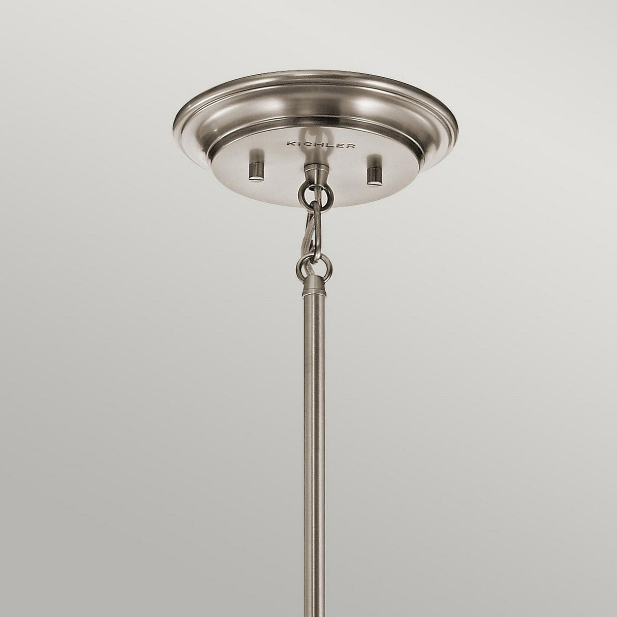 A close-up of the Waverly 1 Light Mini Pendant - Silver, mounted on a ceiling. A metal rod extends downward from the round ceiling mount and is secured by a chain link. The fixture boasts a minimalistic and modern design while exuding a timeless, vintage style appeal with its subtle silver finish.