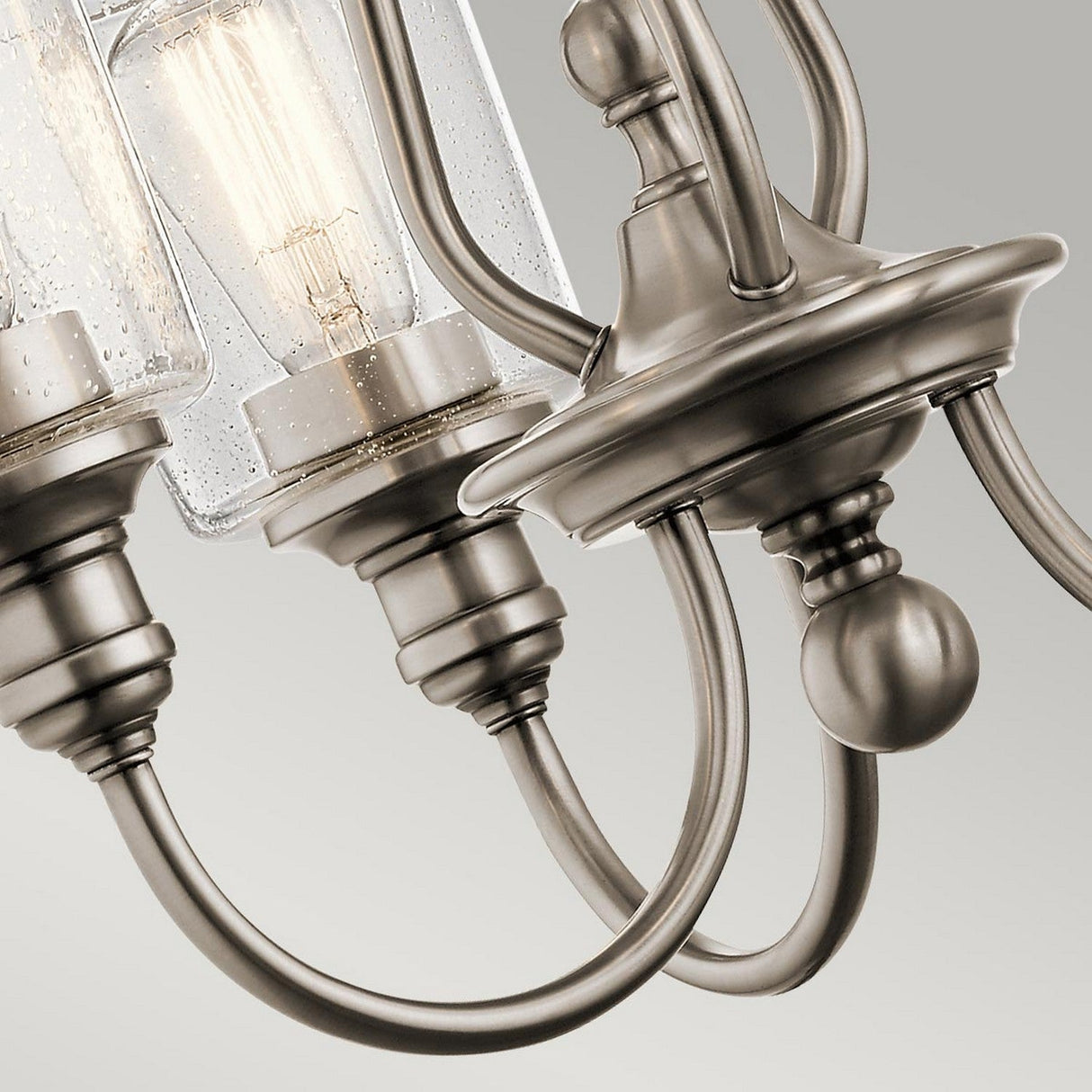 A close-up of the Waverly 3 Light Chandelier - Silver features curved arms and seeded glass shades, showcasing visible vintage-style light bulbs set against a neutral background.