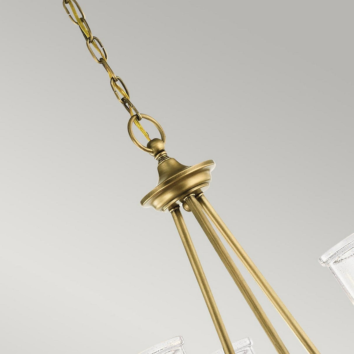 The Waverly 3 Light Chandelier in natural brass showcases vintage elegance with its three gracefully extending arms from a central fixture, suspended by a decorative chain. The seeded glass shades enhance its charm against a light gray background.