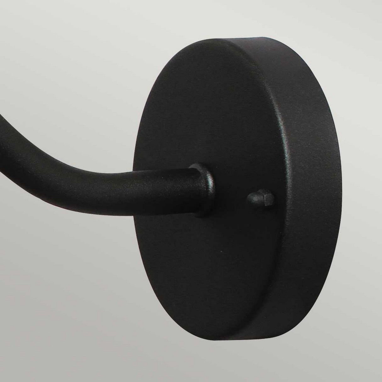 The Klampenborg 1 Light Outdoor Wall Light in black showcases a close-up view with its round form and attached curved arm. The matte-finished wall mount complements the sturdy, slightly textured arm that encapsulates Scandinavian design against a plain, light backdrop.