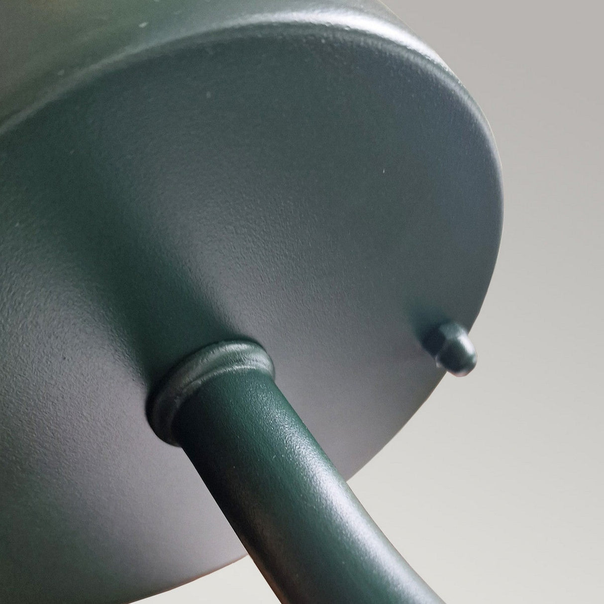 Close-up of the Klampenborg 1 Light Outdoor Wall Light in a dark green metal base featuring a cylindrical shape and a hole for pole attachment, embodying Scandinavian design elegance. Its smooth surface shines against a neutral gray backdrop, making it ideal for an IP44-rated outdoor wall light setup.