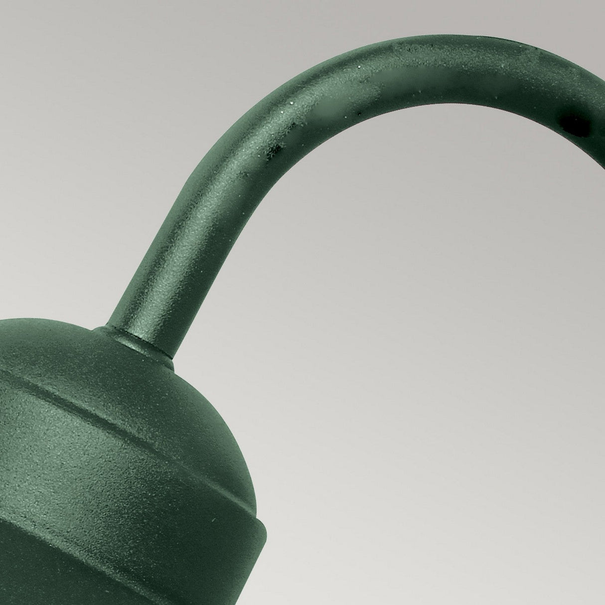 Close-up of a dark green metal watering can spout against a light gray background. The curved handle is visible, showcasing a minimalist and Scandinavian design that echoes the sleek aesthetics of the Klampenborg 1 Light Outdoor Wall Light in green.