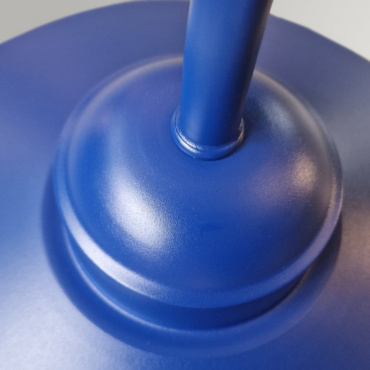 A close-up of the Klampenborg 1 Light Outdoor Wall Light showcases a Scandinavian-inspired design with its smooth, navy blue metallic surface and central cylindrical support. The image accentuates the elegant curves and textures characteristic of this refined outdoor fixture.