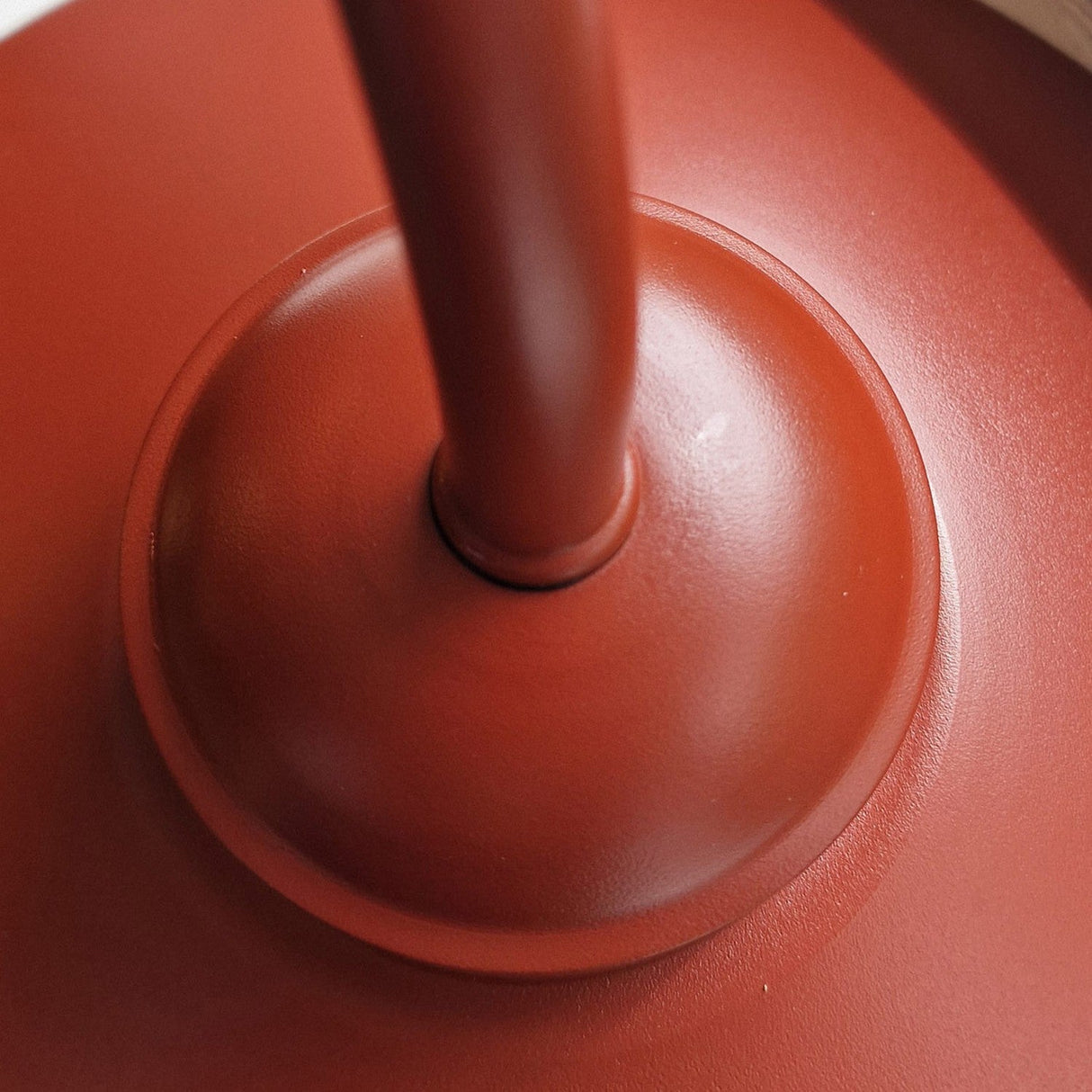 Close-up of the Klampenborg 1 Light Outdoor Wall Light in oxide red, featuring its sleek handle and base with emphasis on the central point where they connect. The image highlights its glossy red finish and circular design, echoing Scandinavian style minimalism.