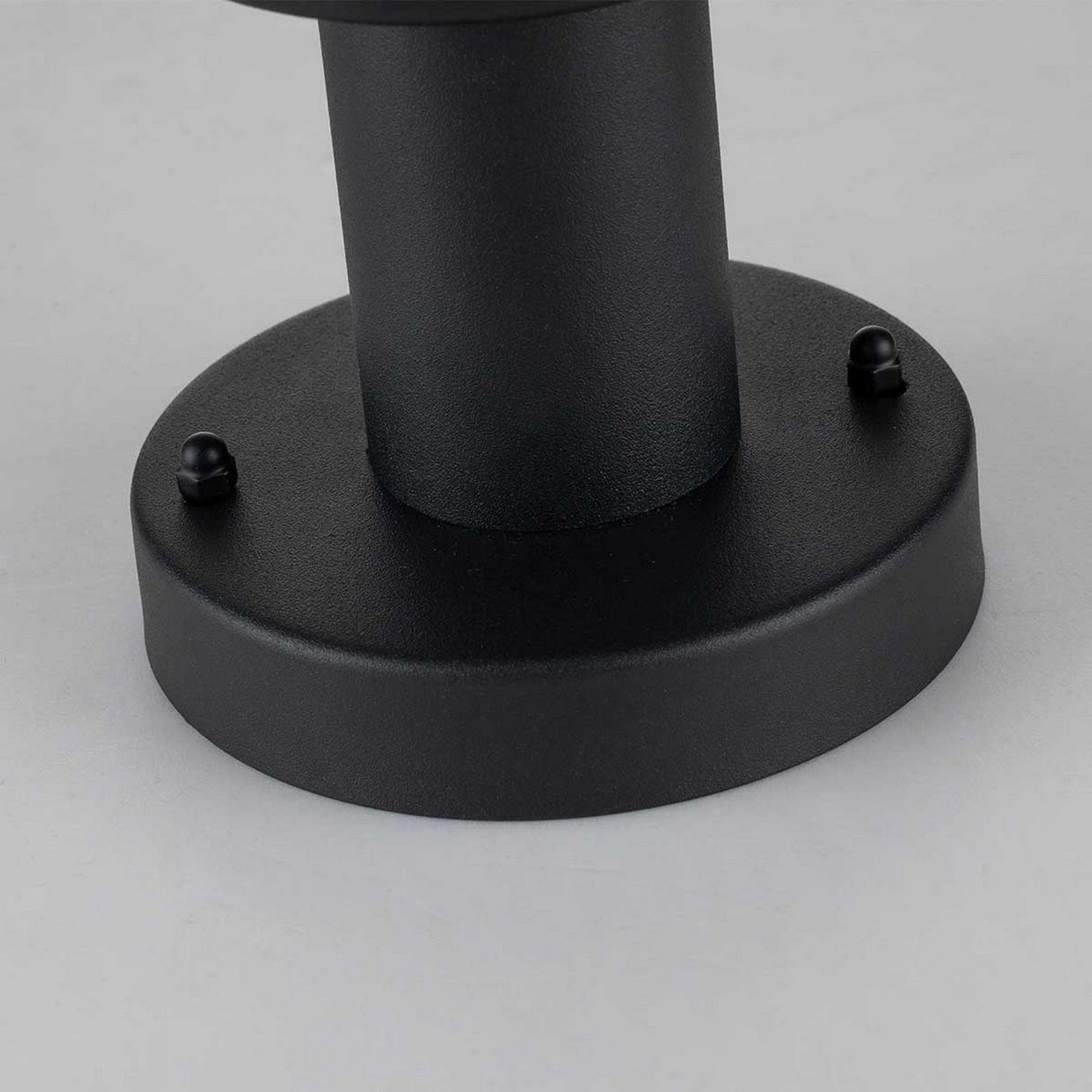 Close-up of a round black metal base with a vertical cylindrical support, echoing Scandinavian design. The Klampenborg 1 Light Pedestal - Black features two small screws on opposite sides, highlighting its sleek outdoor lighting allure against a light gray background.
