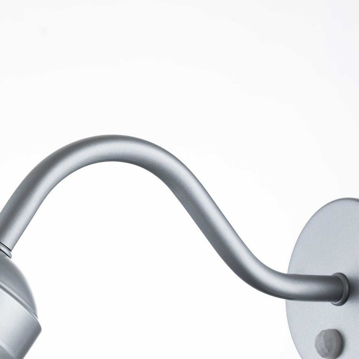 A close-up view of the Klampenborg 1 Light Outdoor Wall Light with PIR in a sleek silver finish showcases its modern design, featuring a curved arm and round base. Its minimalist elegance stands out beautifully against a plain white background, making it an ideal addition to any setting. Additionally, it's equipped with a PIR sensor for enhanced functionality.