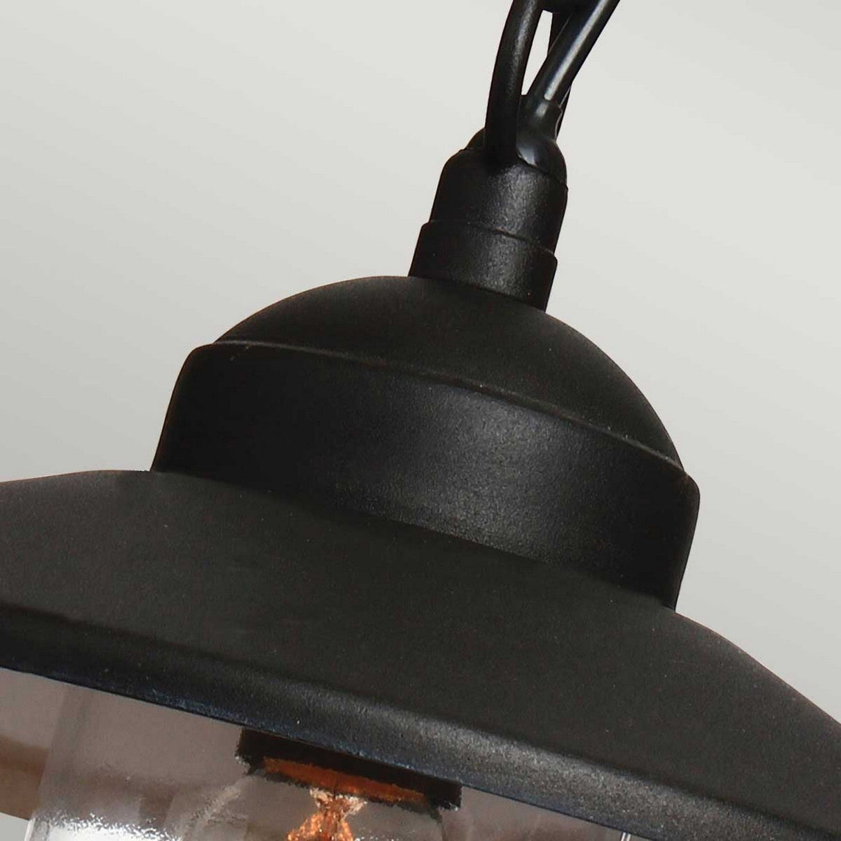 A close-up of the Klampenborg 1 Light Outdoor Chain Pendant - Black showcases its IP44-rated design with a domed top. This Scandinavian-inspired lantern features a clear glass shade that reveals an exposed bulb and is suspended by a black cord, against a neutral light grey background.