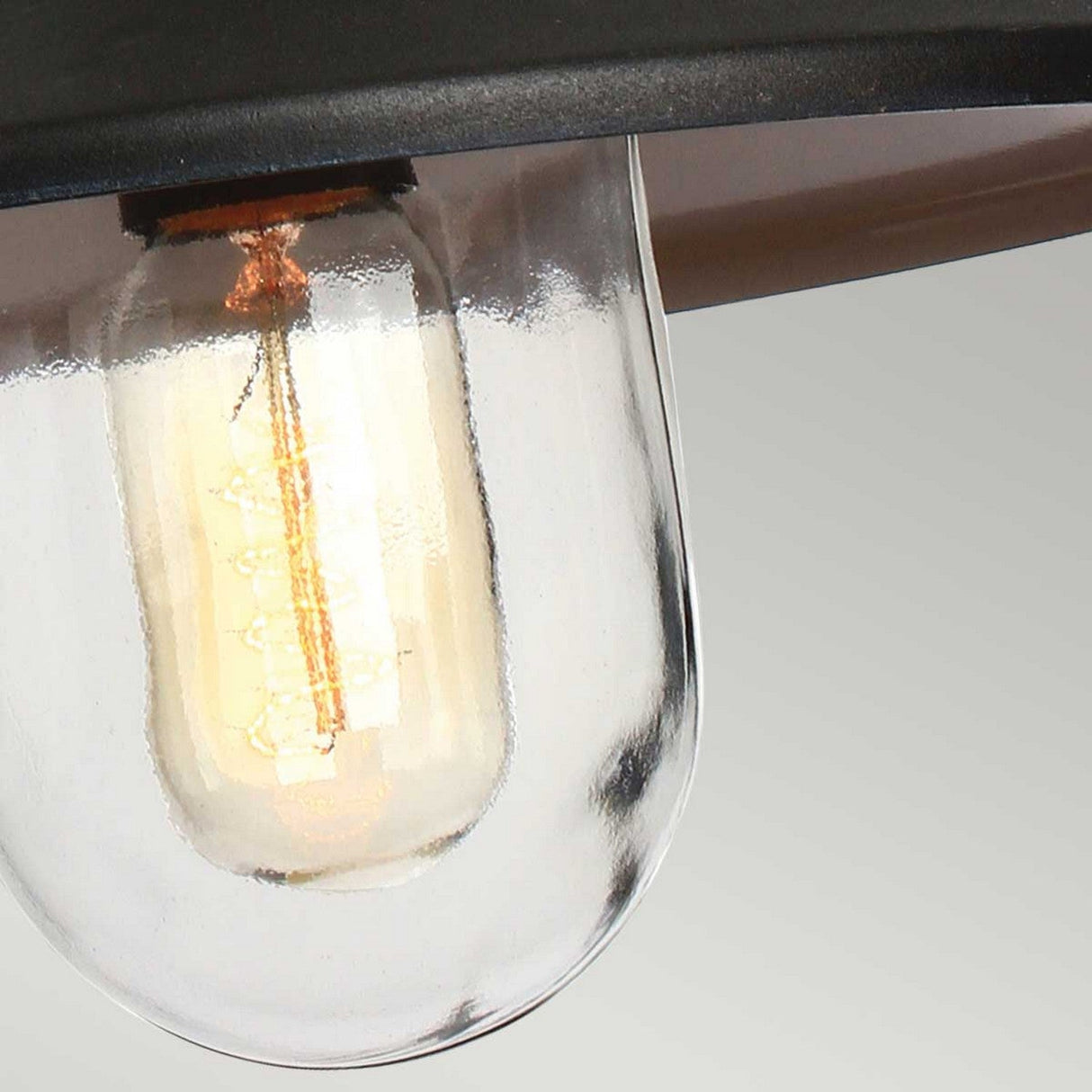Close-up of the Klampenborg 1 Light Outdoor Chain Pendant - Black featuring a glowing filament within a clear glass cover, similar to a Scandinavian lantern, set against a light gray background.